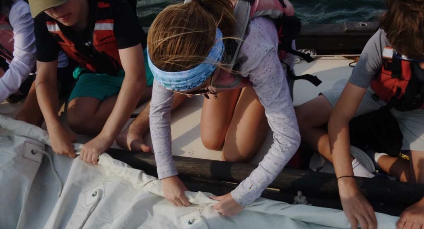 Three people wearing life jackets work to fold a sail.